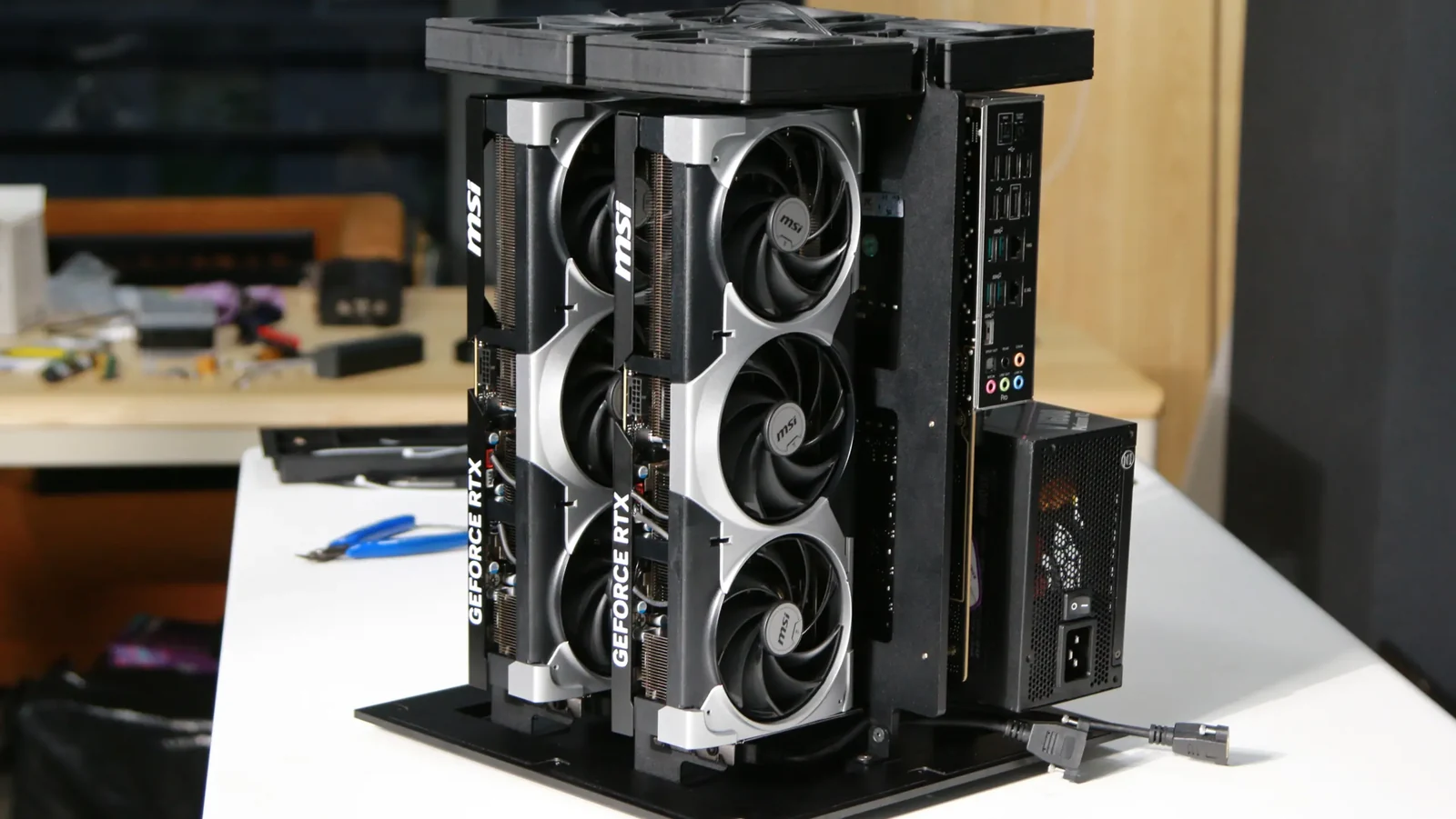 Open-frame concept computer with two vertically mounted NVIDIA GeForce RTX 5090-class graphics cards, compact motherboard, power supply, and top-mounted fans.